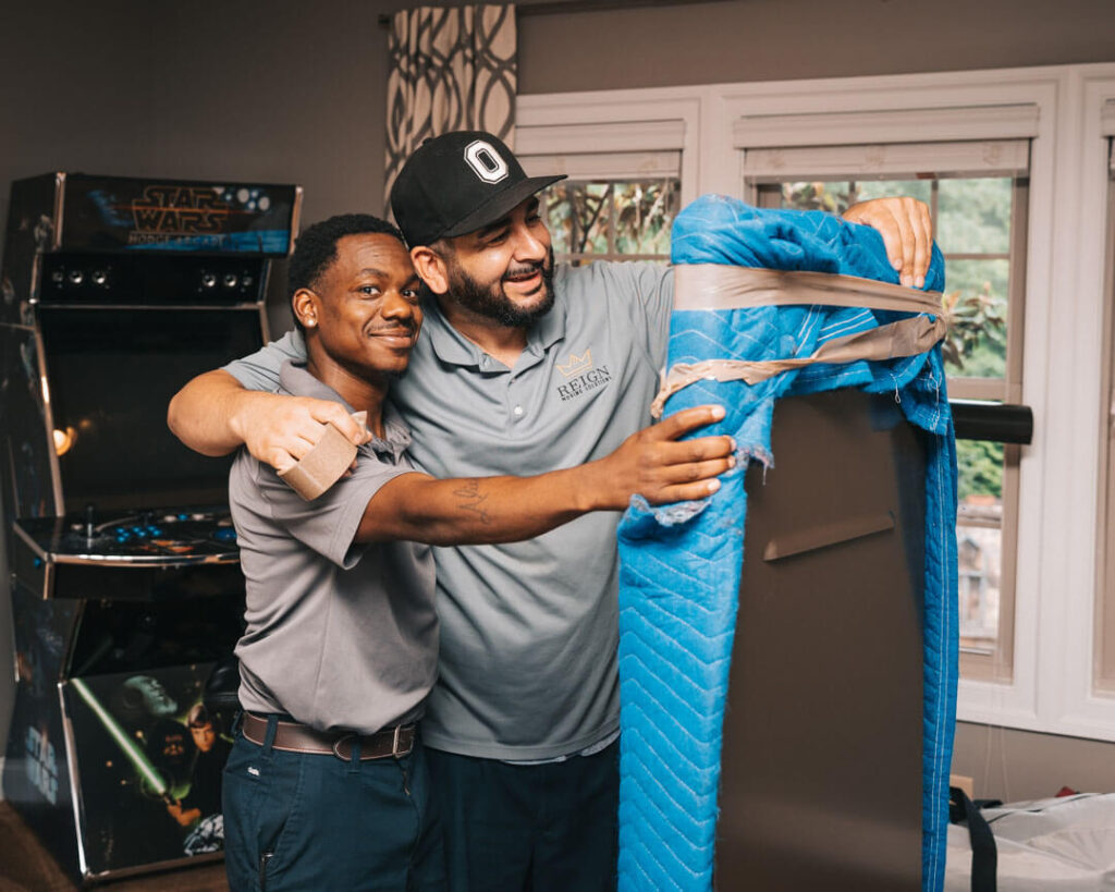 Two men smiling while moving items into a house