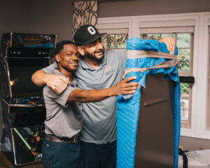 Two men smiling while moving items into a house